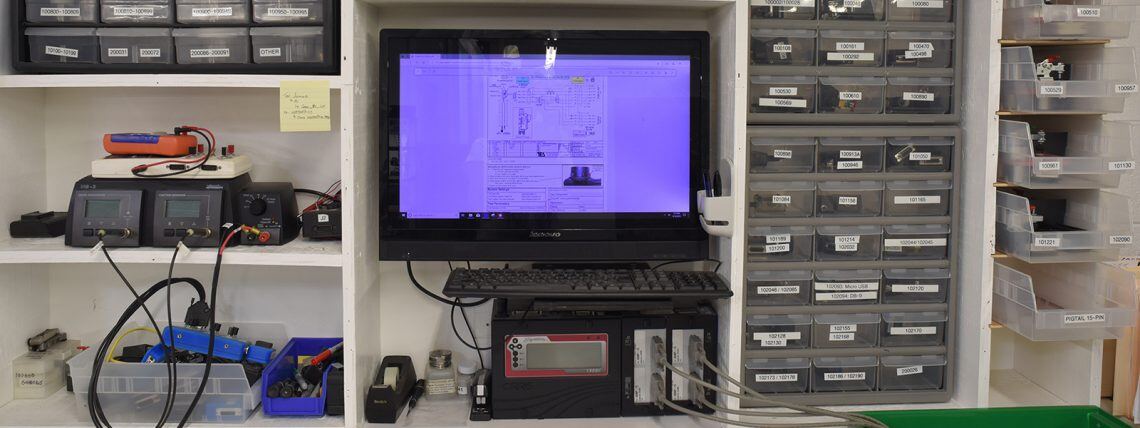 DEM engineering bench with test equipment, a drawing on screen and parts bins